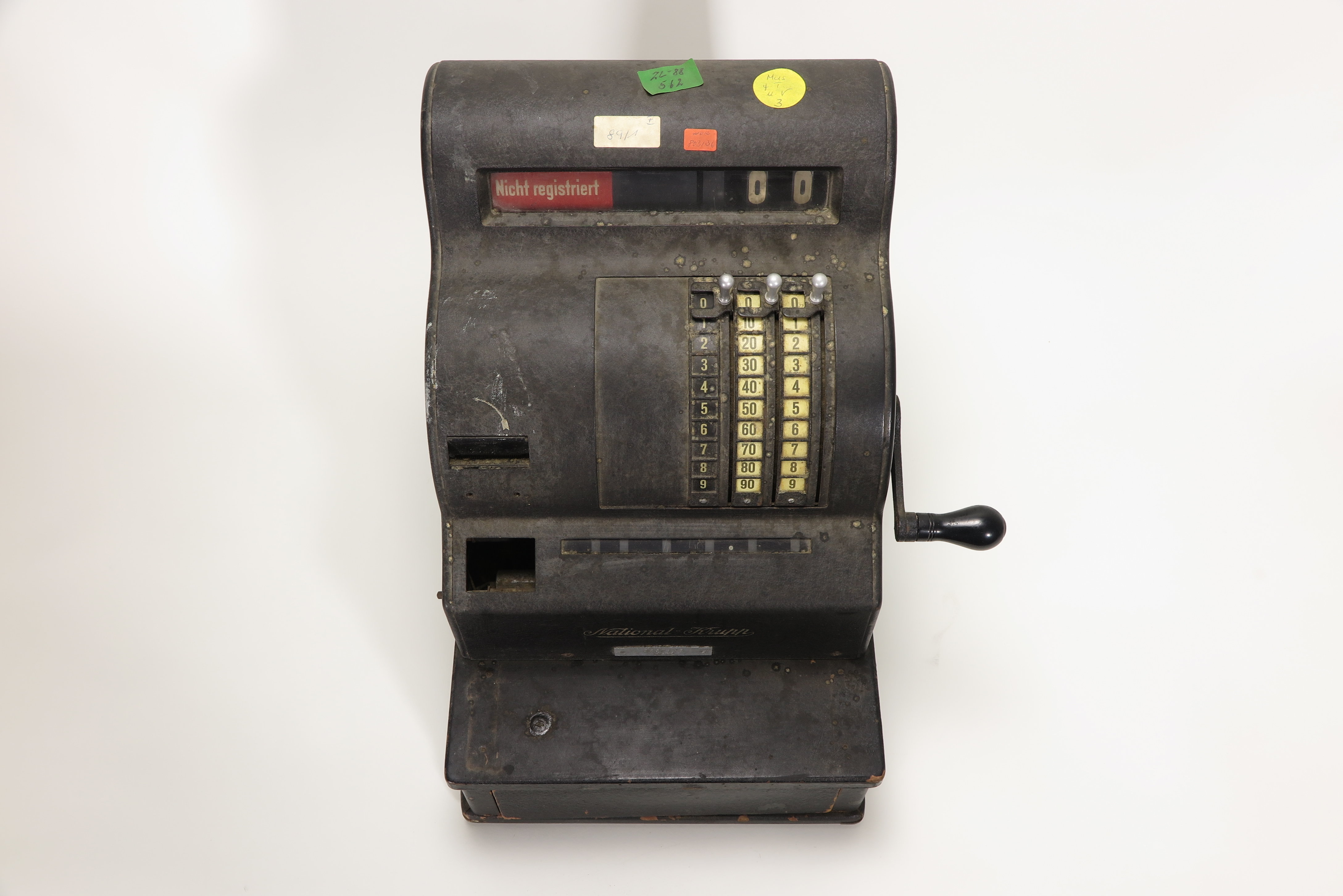 A cash register from the 1930s with four colored KuA stickers. The stickers feature numbers and letters.