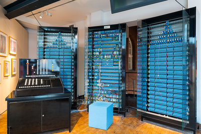 Die drei Speicherschränke des Nachbaus des Zuse-Computers Z3 sind jeweils 2,20 Meter hoch und 1,20 Meter breit und mit insgesamt 1.600 blauen Schaltrelais bestückt. Links im Vordergrund steht die schwarze Bedienkonsole mit vielen Zahlen- und Funktionstasten.