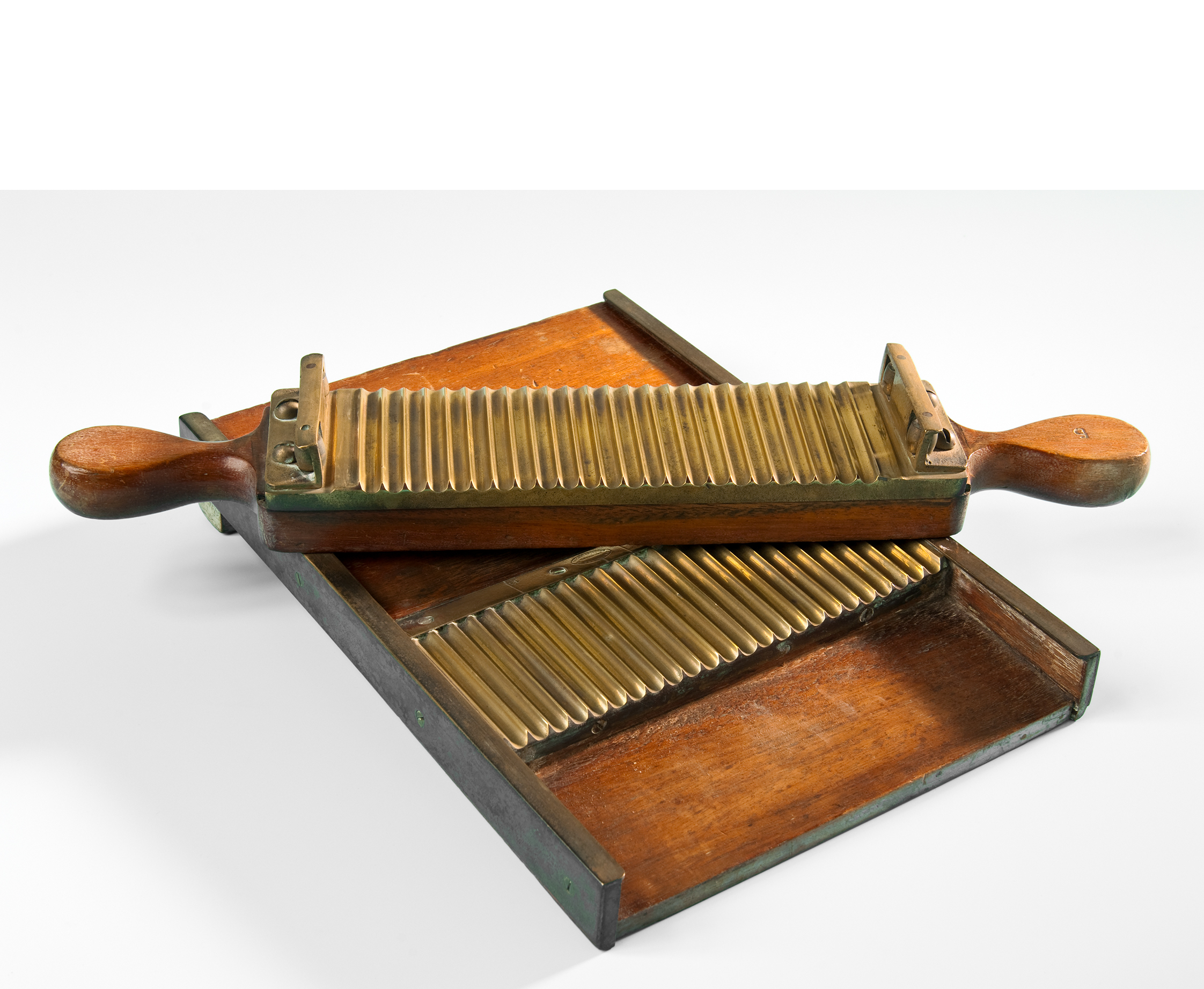 The wooden pill board has a grooved surface. A wooden handle, also grooved, rests on top of it. The handle was used to carefully roll the dough-like mixture of medicine over the grooves. This produced uniform individual portions.