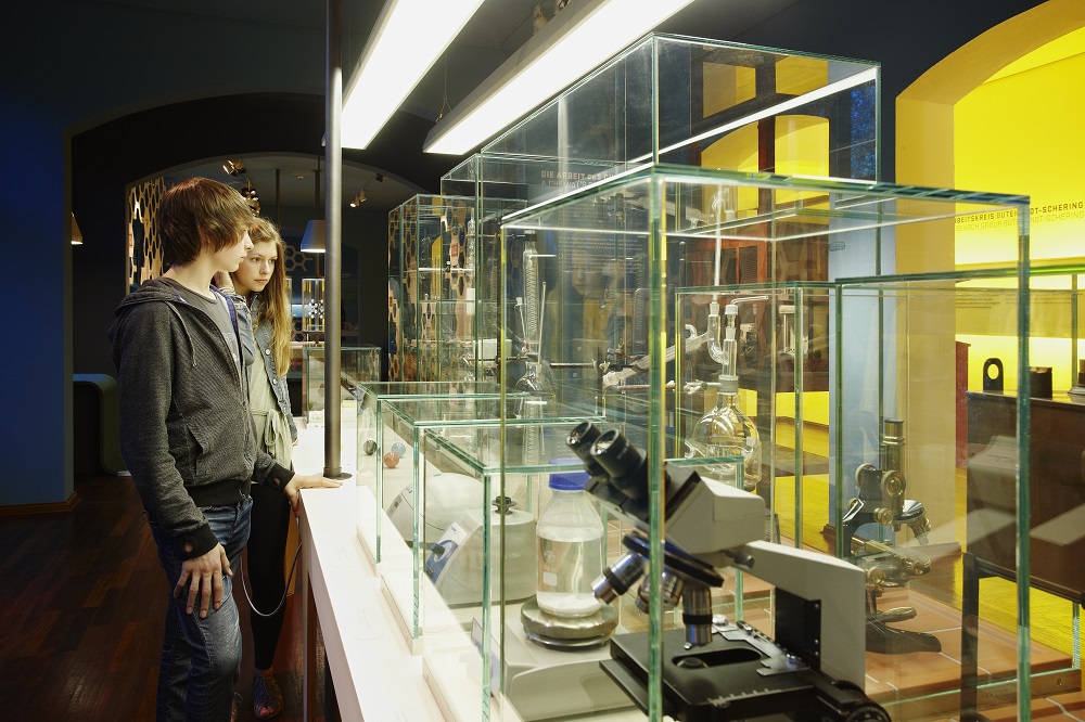 A boy and a girl are standing next to a display case containing microscopes and other equipment.