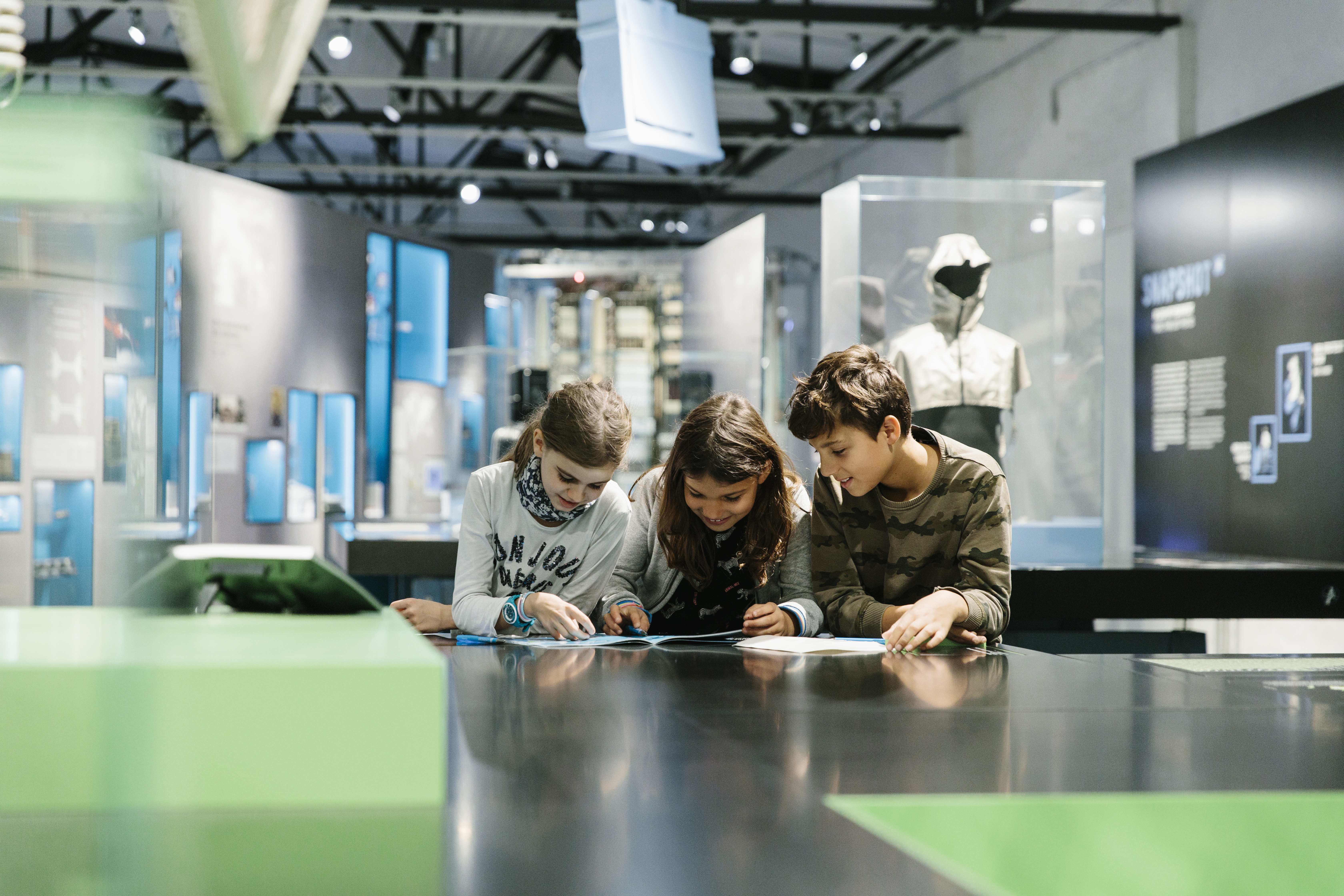 Three children at the Network exhibition, exploring the exhibition with the interactive booklet.