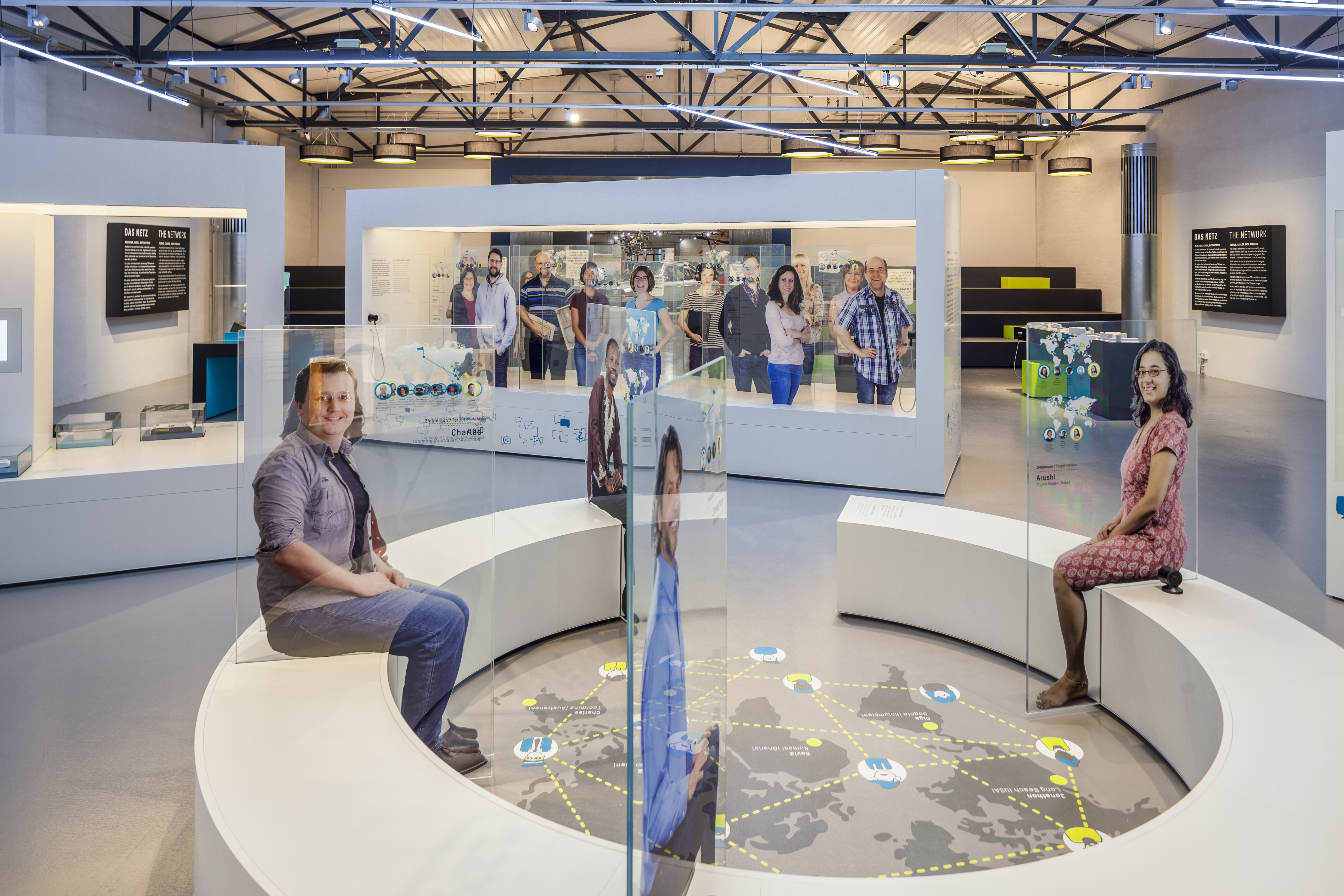 In the center of the CONNECT exhibition area stands a circular bench. Attached to it are glass panels featuring life-size depictions of various people. Inside, there is a floor graphic depicting a world map.