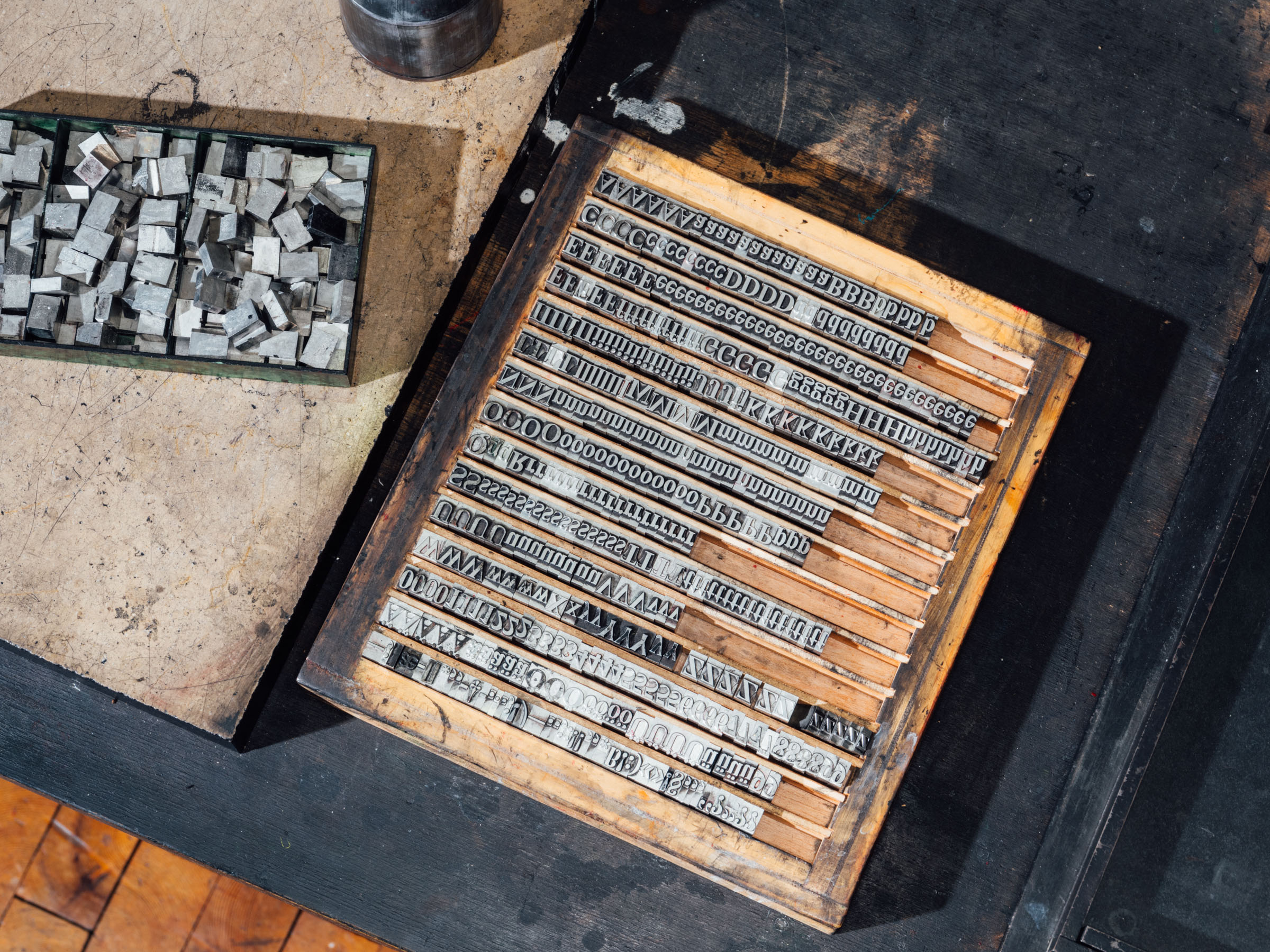  Metal letters are arranged into sentences in a wooden box with individual horizontal rows. Next to it is a box of loose letters.