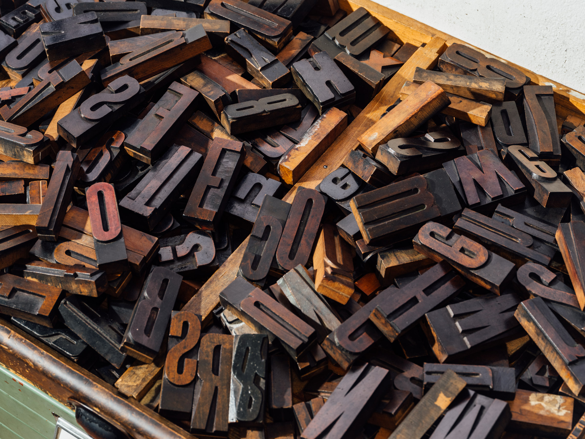 Individual metal letters lie jumbled together in a wooden box.