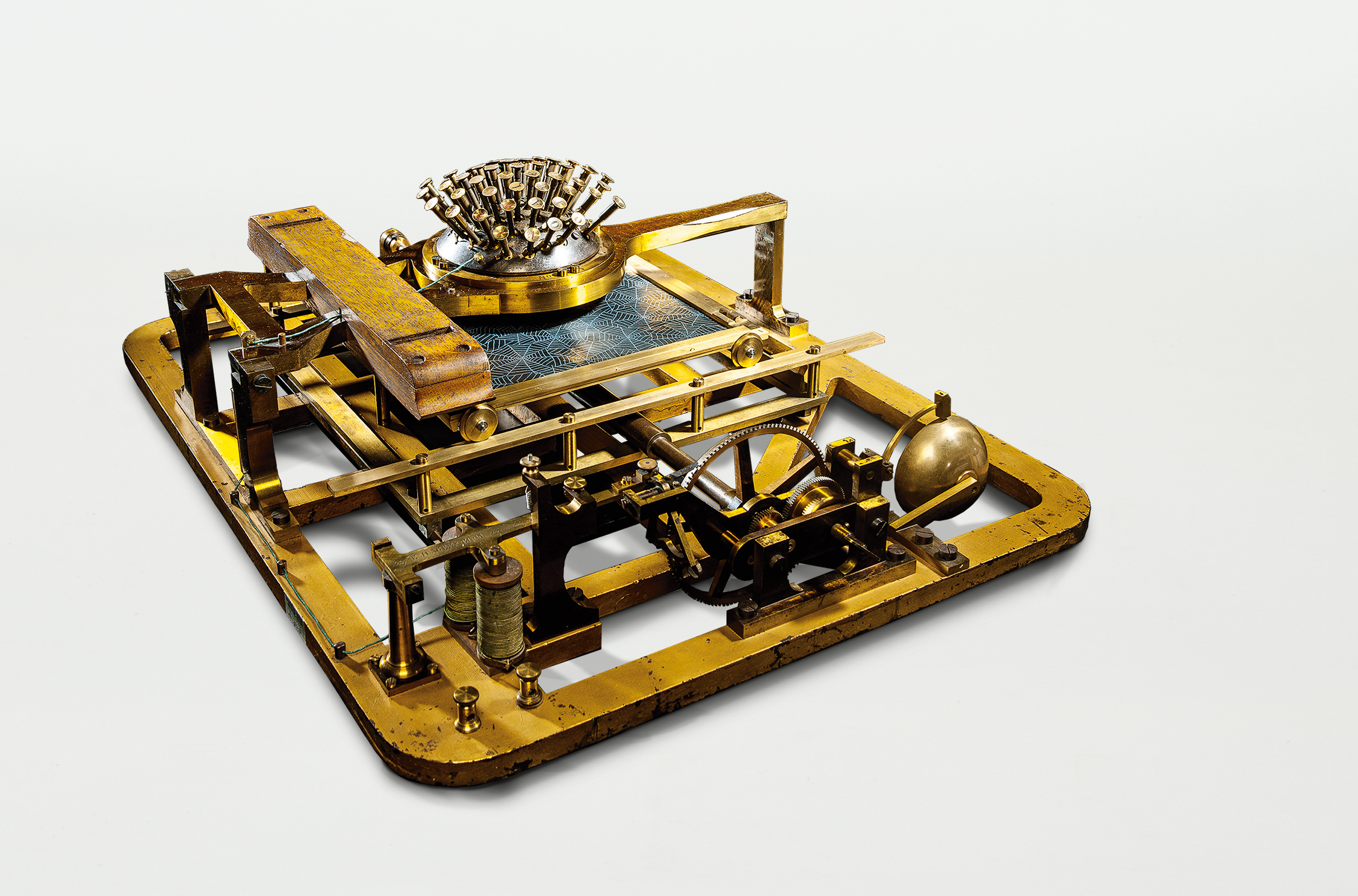 This typewriter is approximately 75 centimeters long, 60 centimeters wide, and 30 centimeters high. The keys are arranged concentrically on a hemisphere at the top center. The keys and the machine parts are made of metal.
