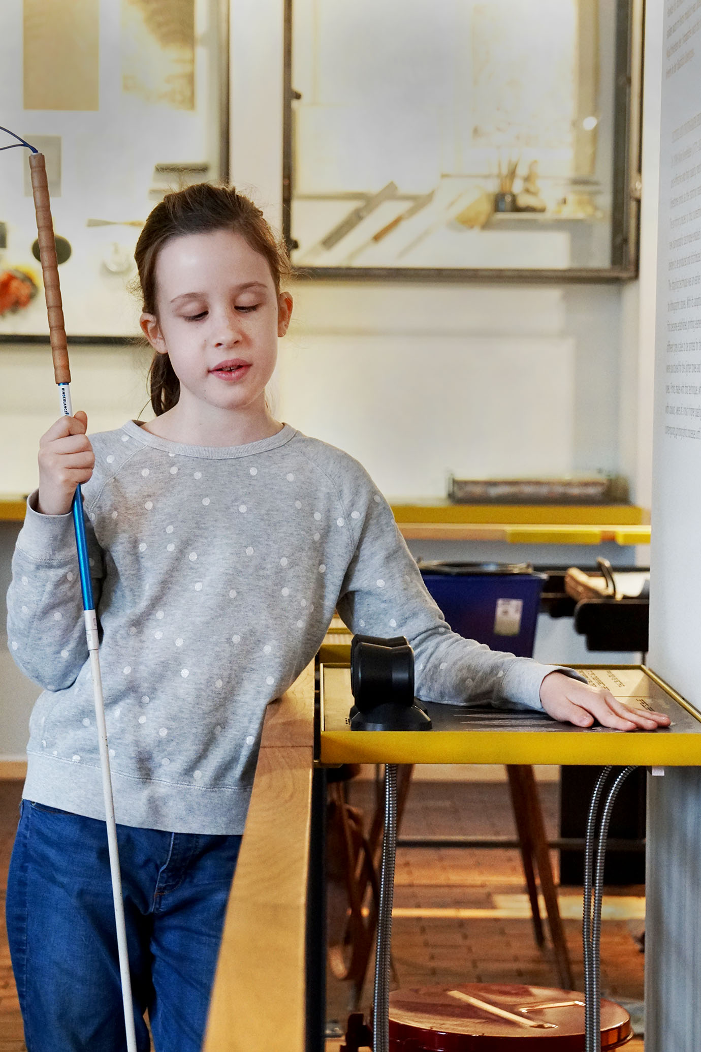 A girl is holding a white cane in her right hand. With her left hand, she is exploring the tactile exhibit “Nature as a Printer.”