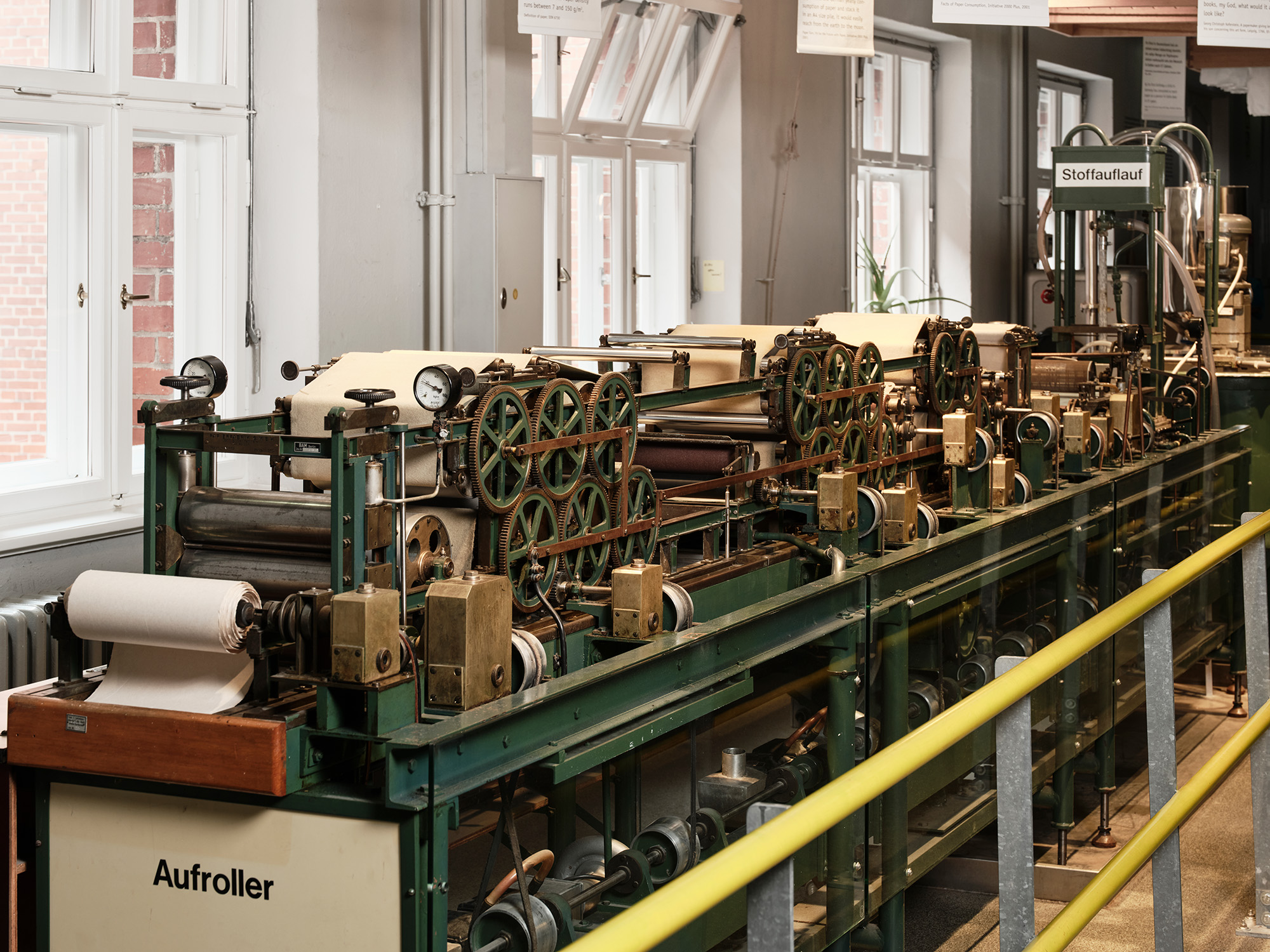 The machine resembles a workbench several meters long. Mounted on it is a system of more than 15 rollers of various sizes through which the paper web passes.