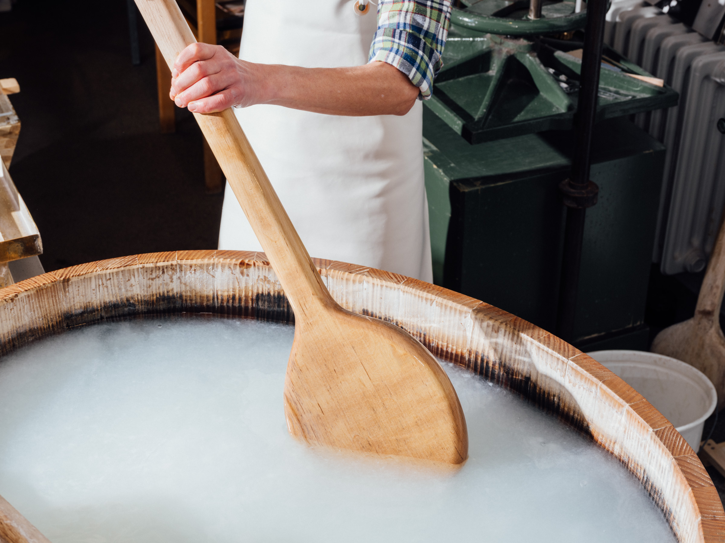 A large wooden spoon in a wooden tub, with a milky-white liquid floating in it.