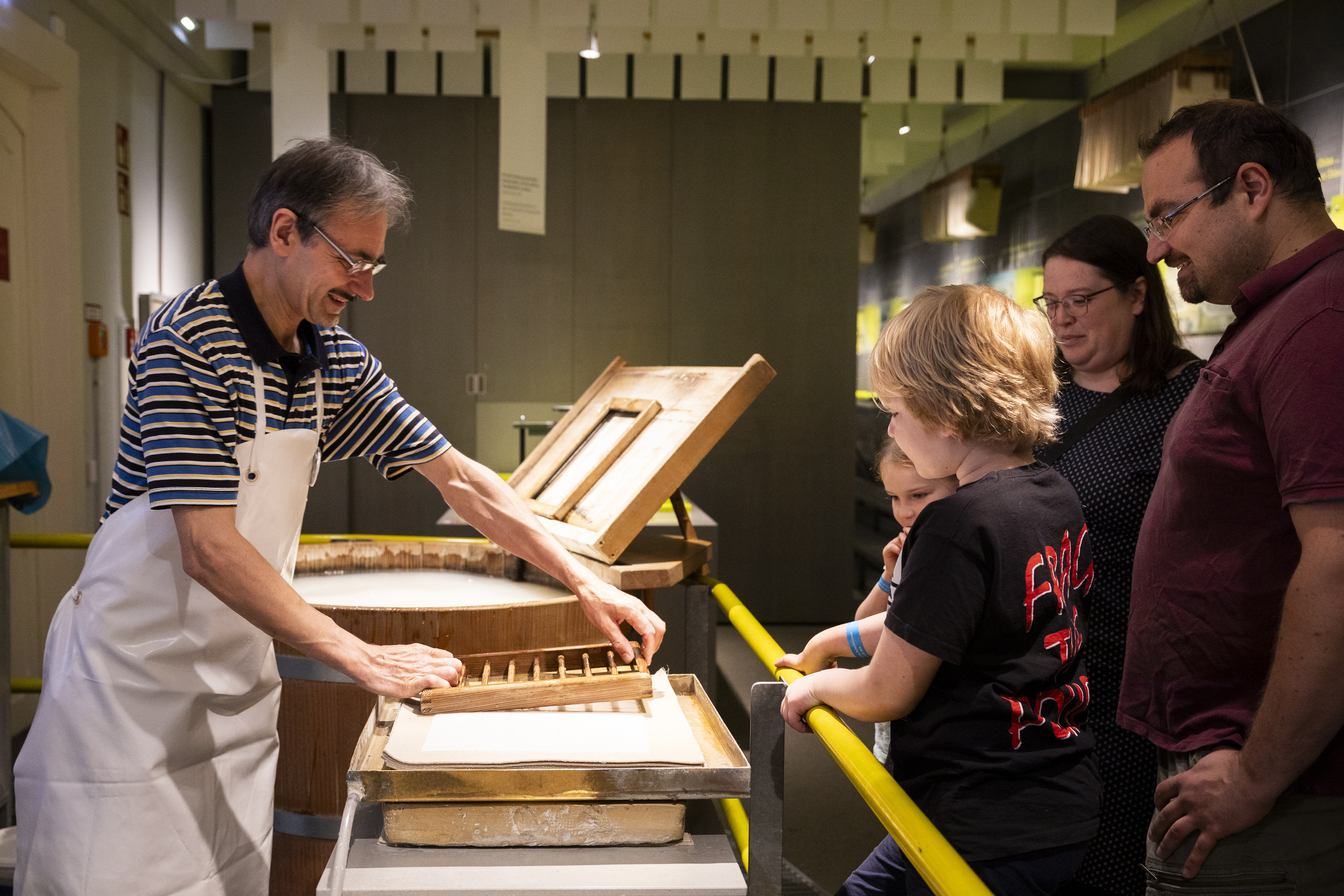A man is pressing a wooden frame onto a stand. Spectators are gathered around him.