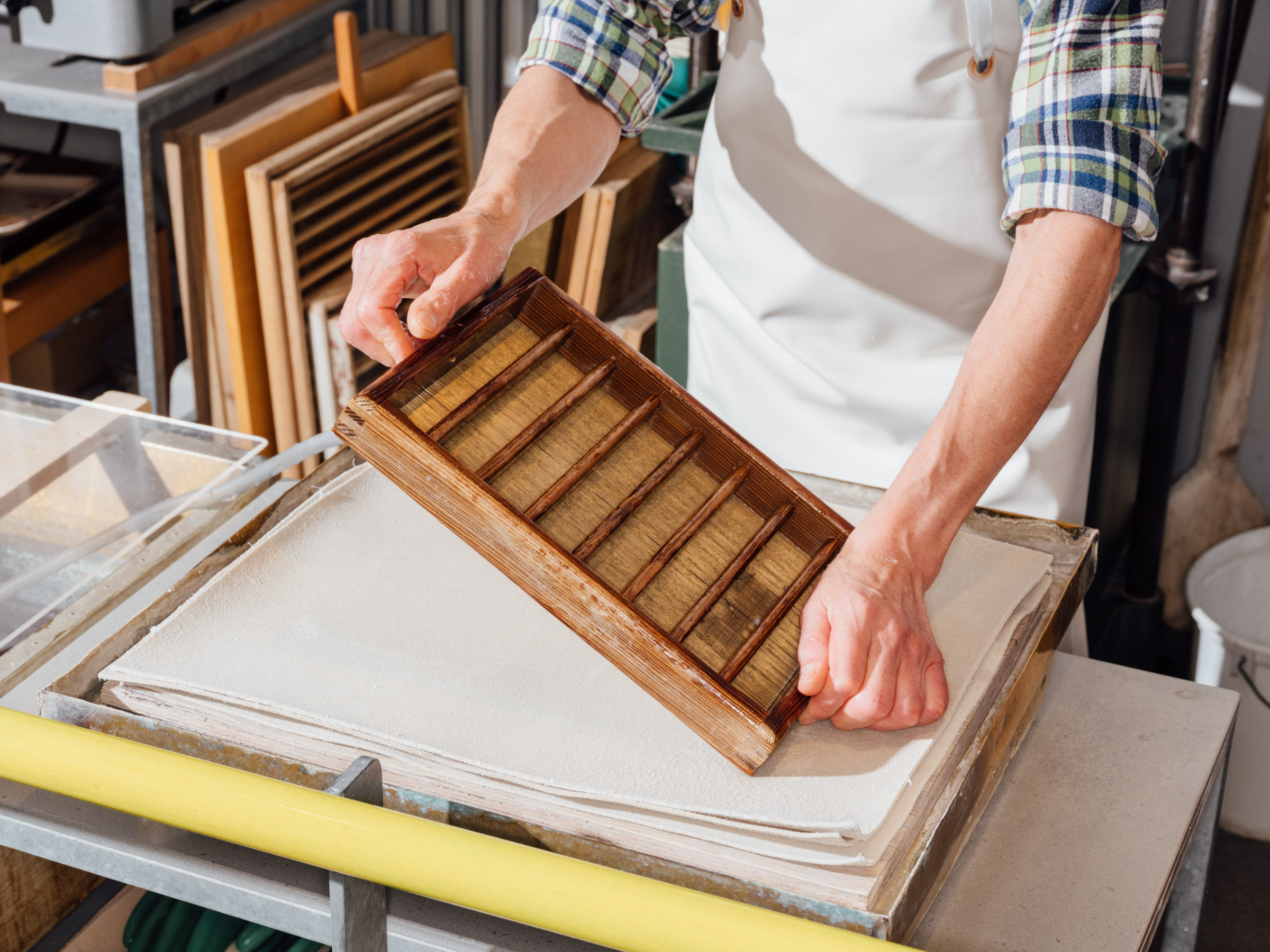 A man is pressing a sheet of freshly pressed paper using a ribbed wooden box.