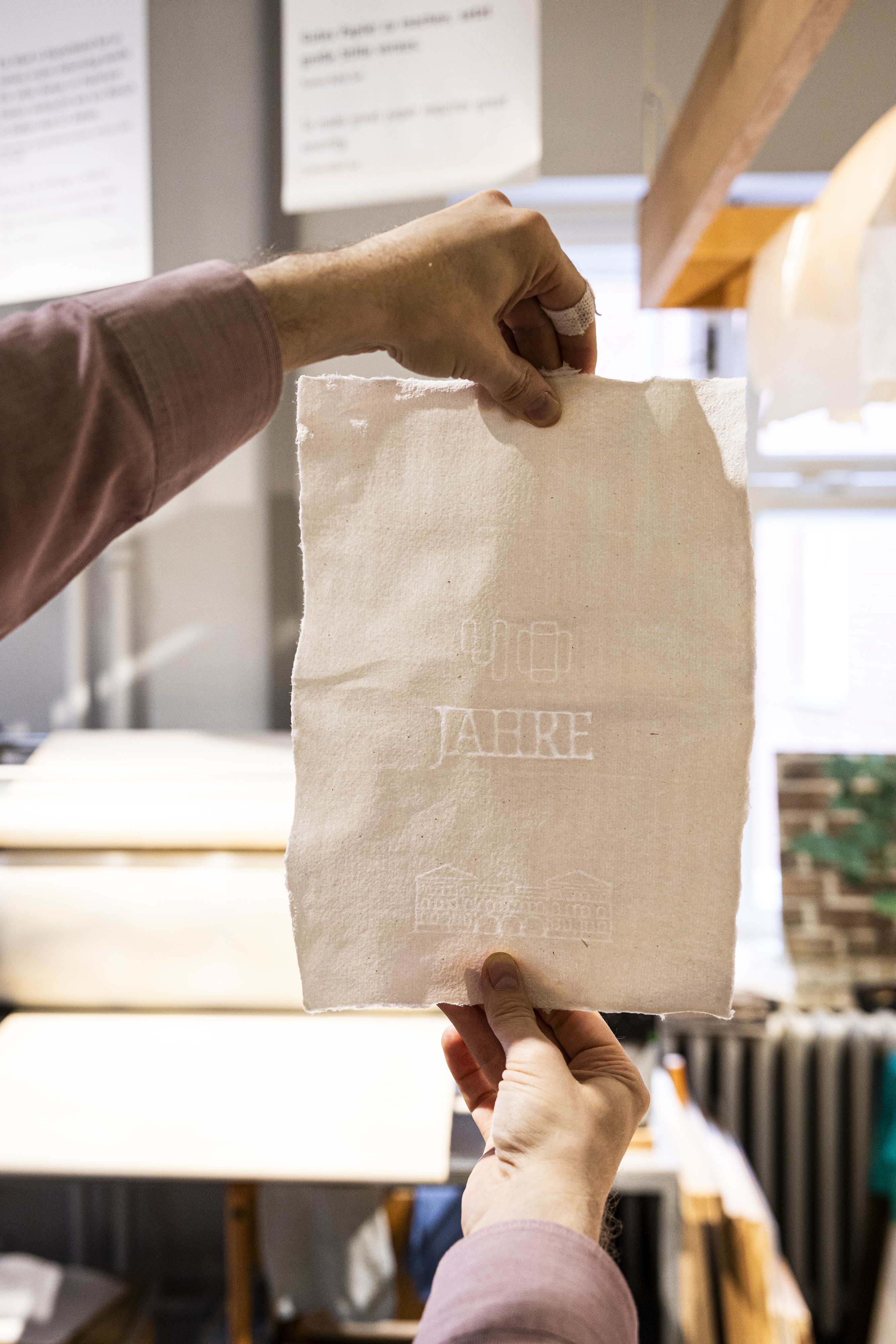A sheet of paper is held up to the light. A watermark can be seen on it.