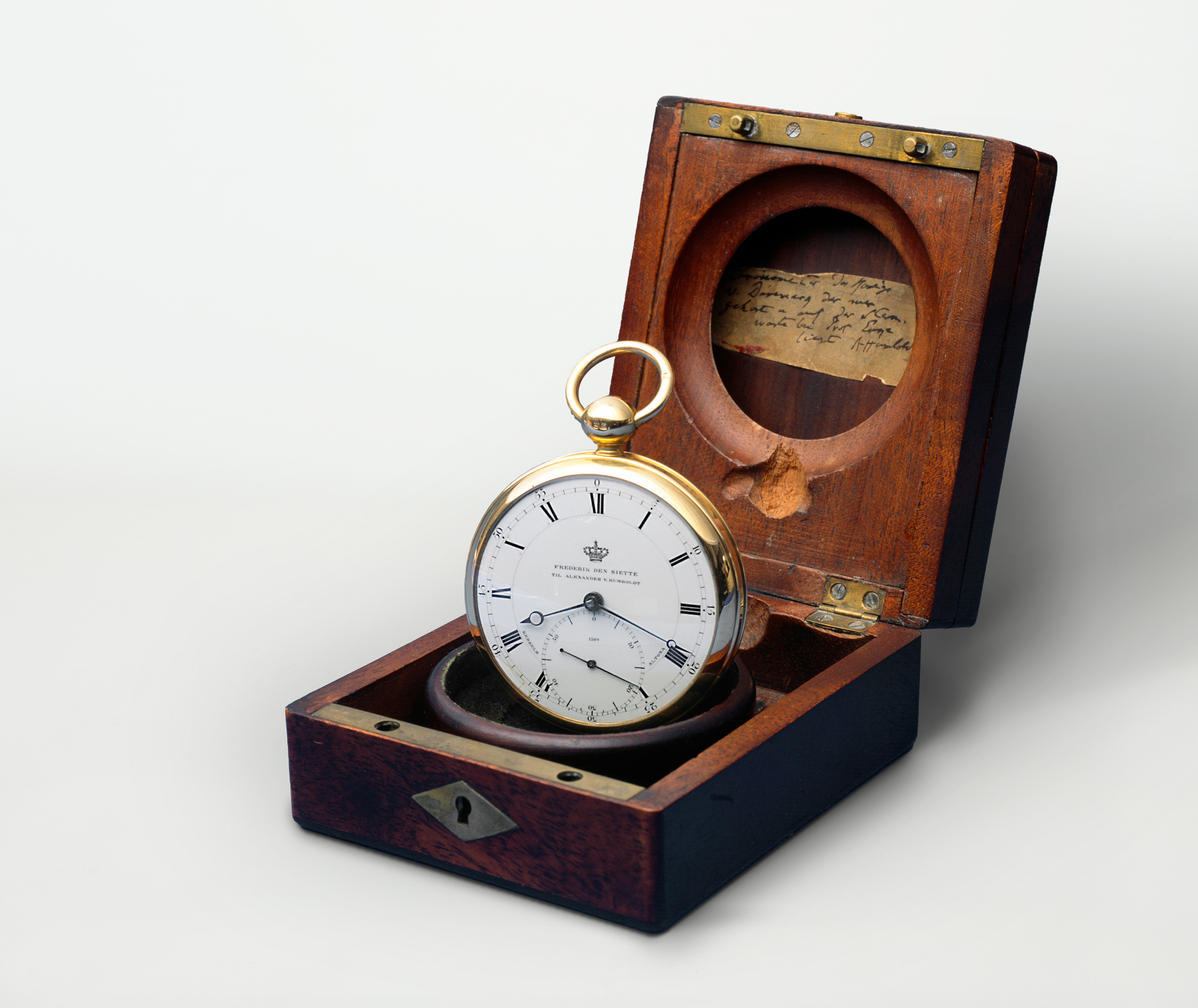 The Humboldt chronometer is a pocket watch with a white dial. The watch is displayed upright in its wooden case.