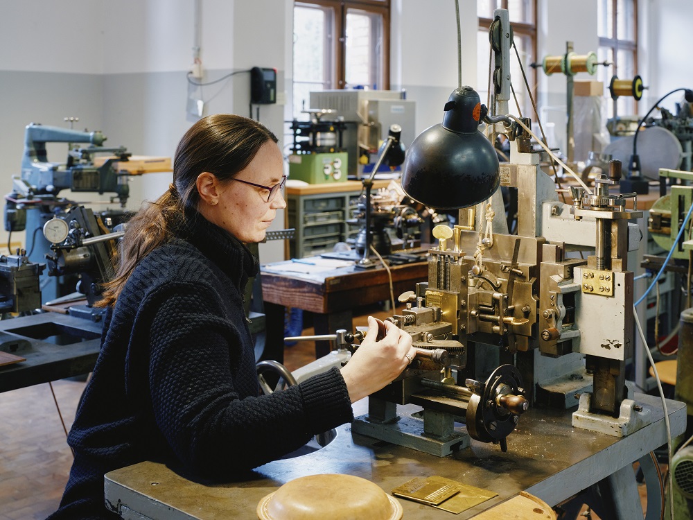 A woman is working on a machine that etches geometric shapes into pieces of metal.
