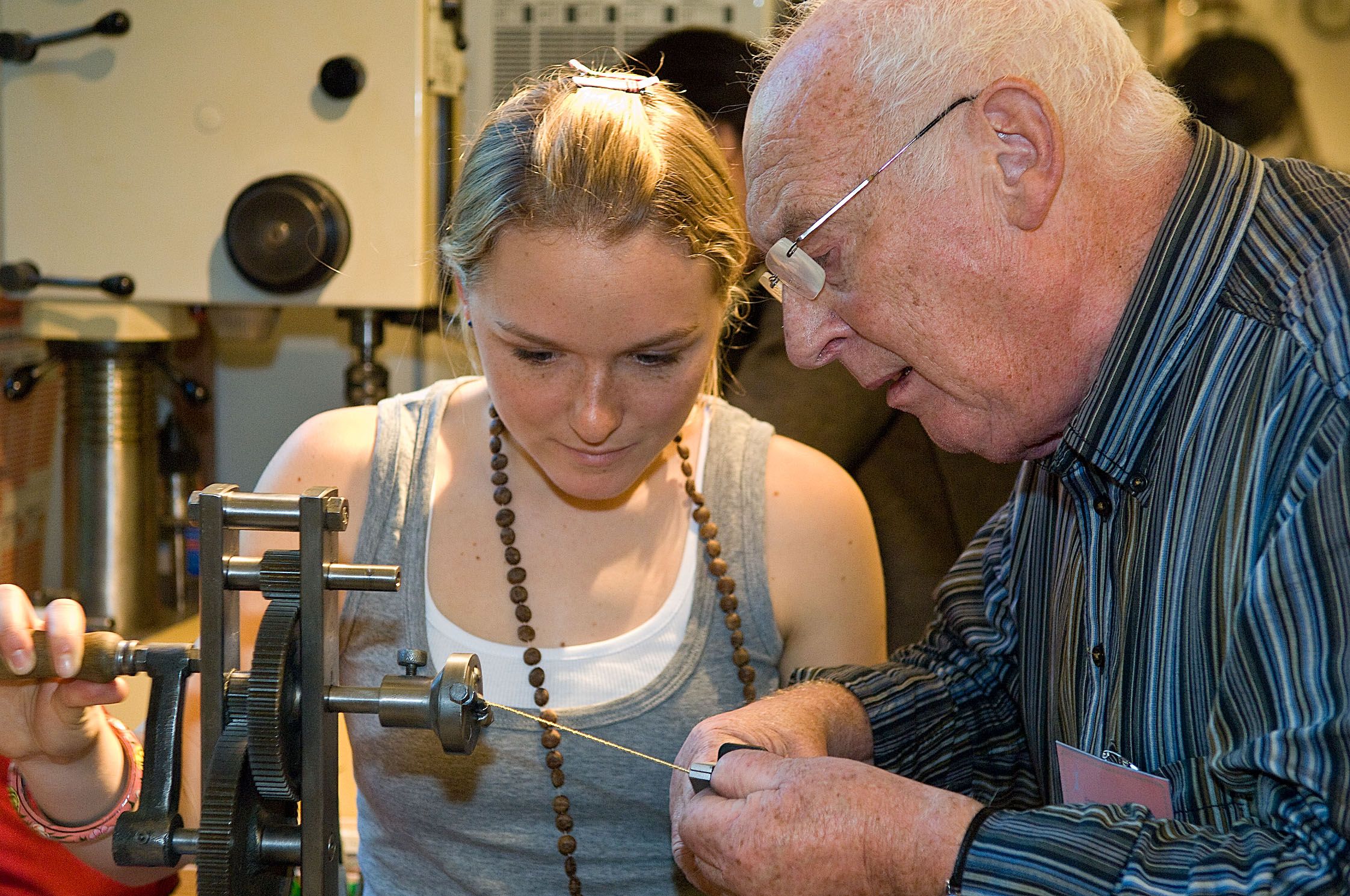 An older man is showing a young woman how to operate a machine that makes lollipops.