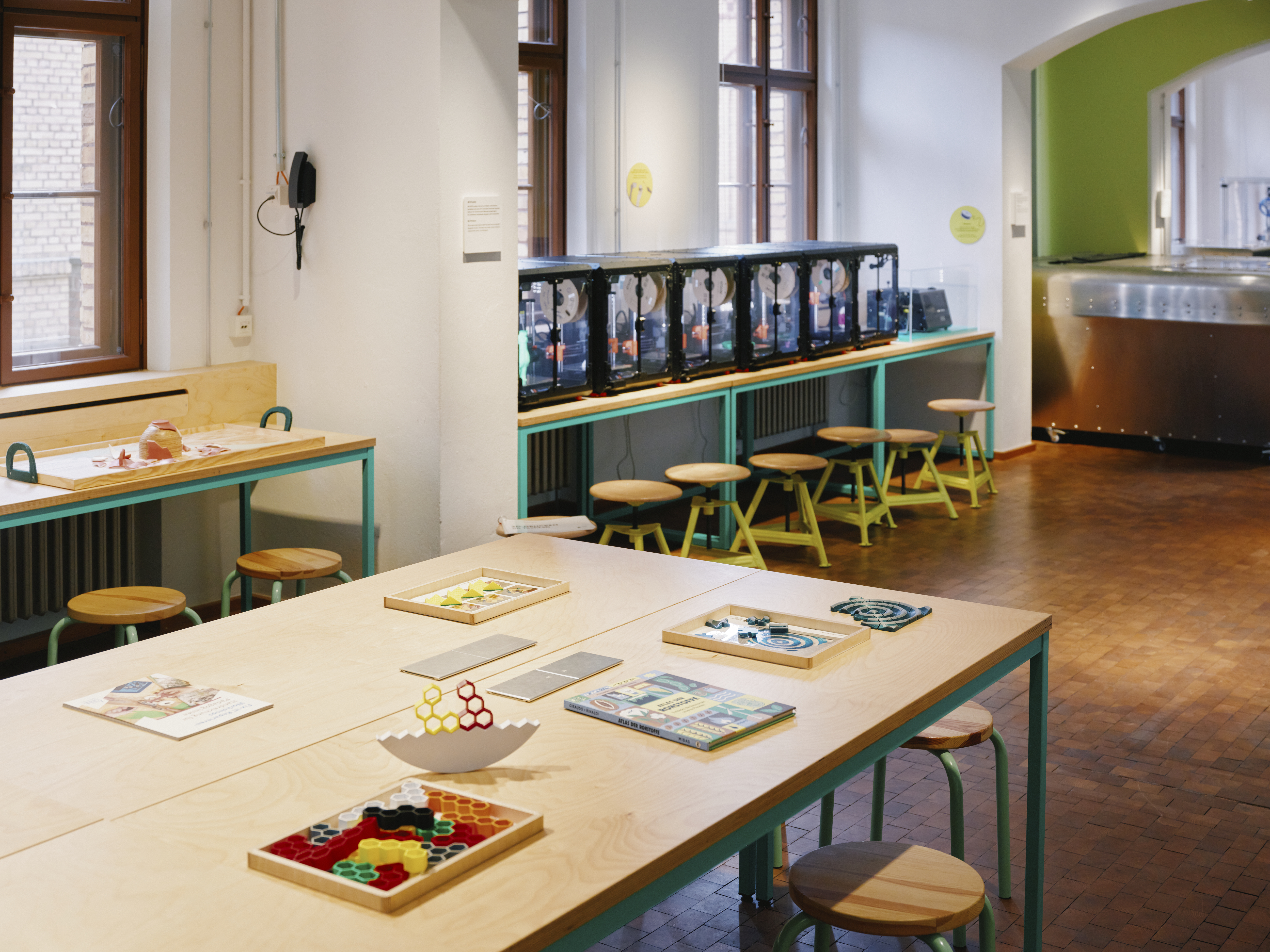 A bright, welcoming room with tables for group work and a row of 3D printers along the wall.