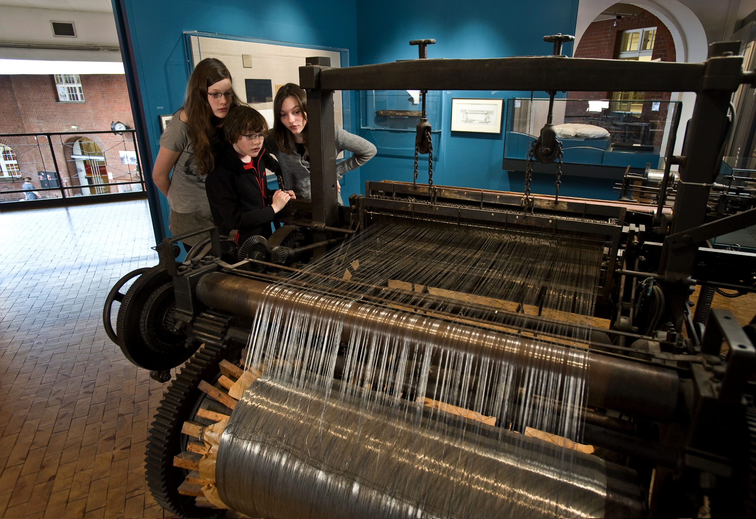 Three children are looking at a large, historic wire loom in the exhibition. 