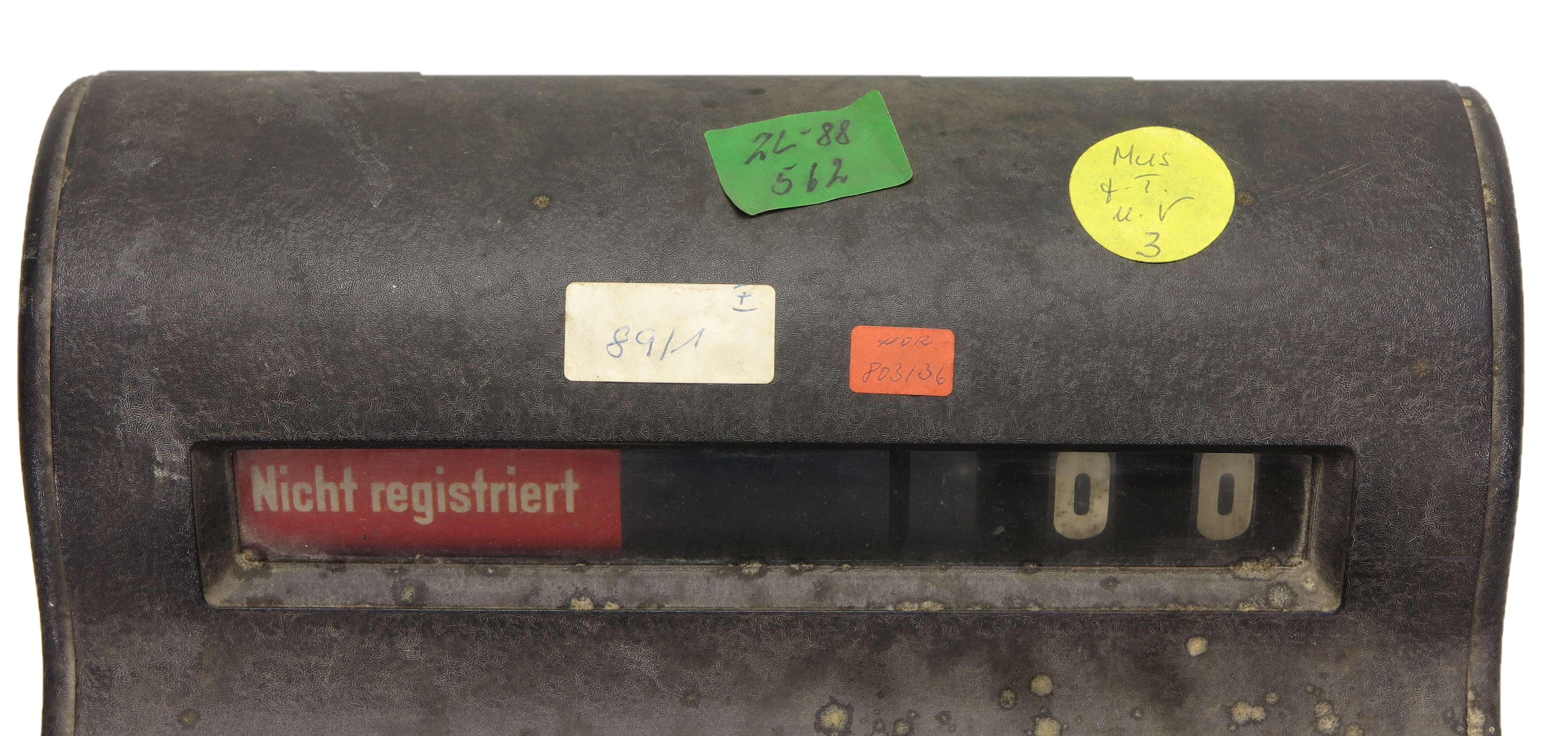 The top part of a cash register from the 1930s with four colored KuA stickers. The stickers feature numbers and letters.
