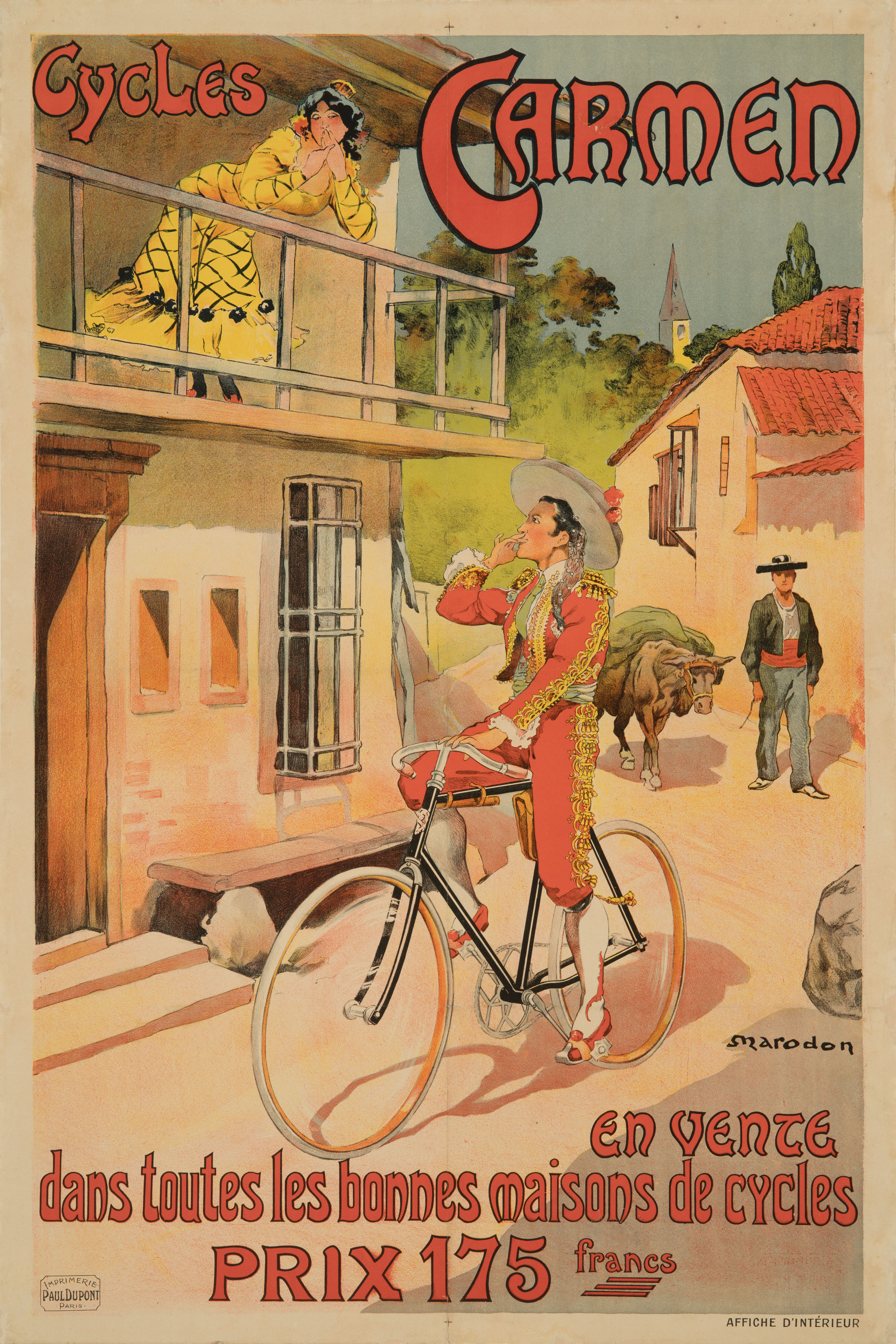 The poster depicts a scene in a Spanish village. On the left is a house. On its balcony stands a Spanish woman in a yellow-and-black dress. She is leaning on the balustrade and looking coquettishly at the viewer. She is framed by the lettering “Cycles Carmen.” In front of the house, a Spanish man in a red-and-gold traditional costume is riding a black bicycle. He looks up at the woman and blows her a kiss. In the background, a Spanish farmer can be seen with a yoke of oxen.