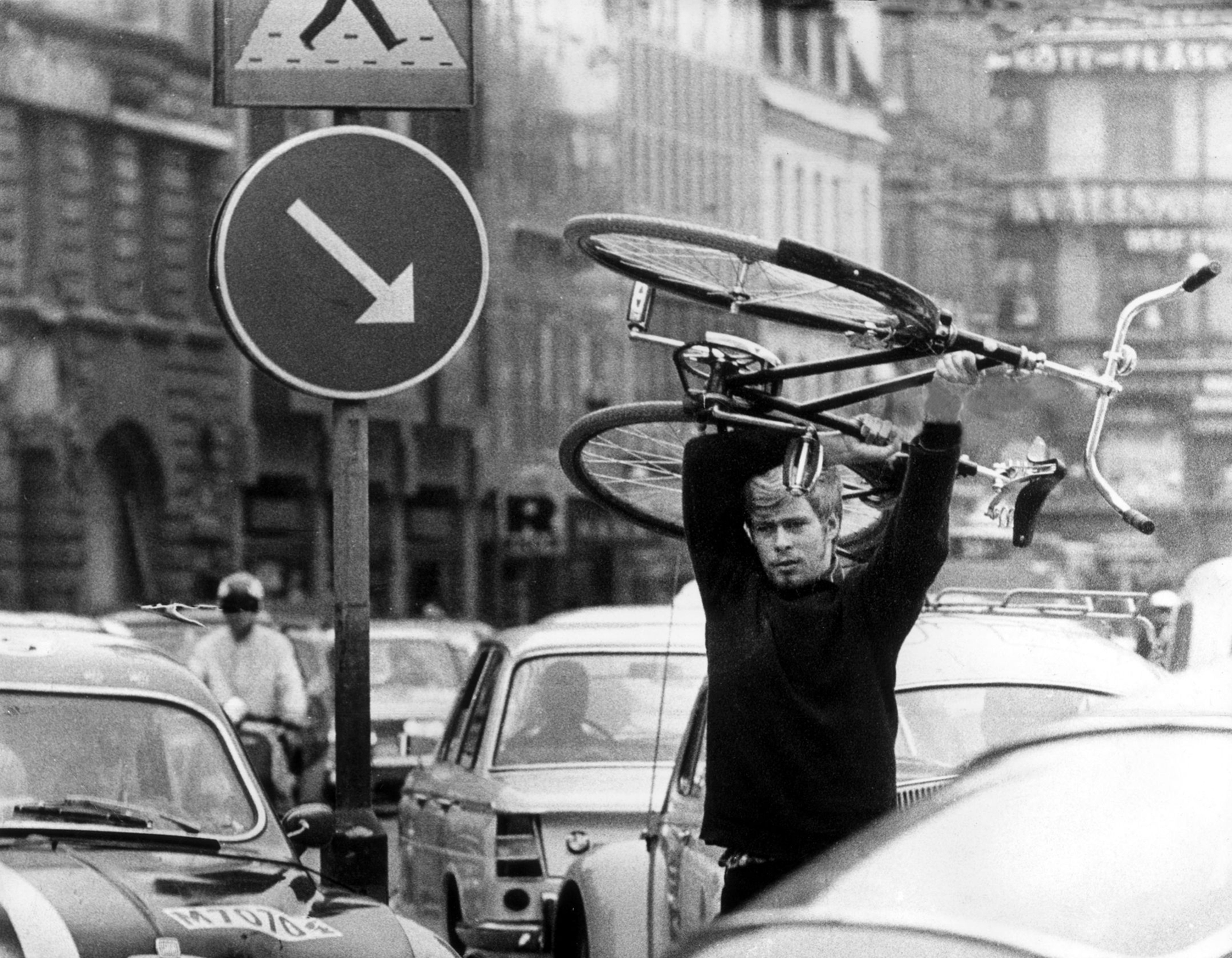 A man is carrying a bicycle over his head. He is walking between cars stuck in traffic. The black-and-white photo was taken on September 3, 1967, in Malmö. On that day, Sweden switched from driving on the left to driving on the right. In some parts of the country, this initially led to problems and traffic jams.