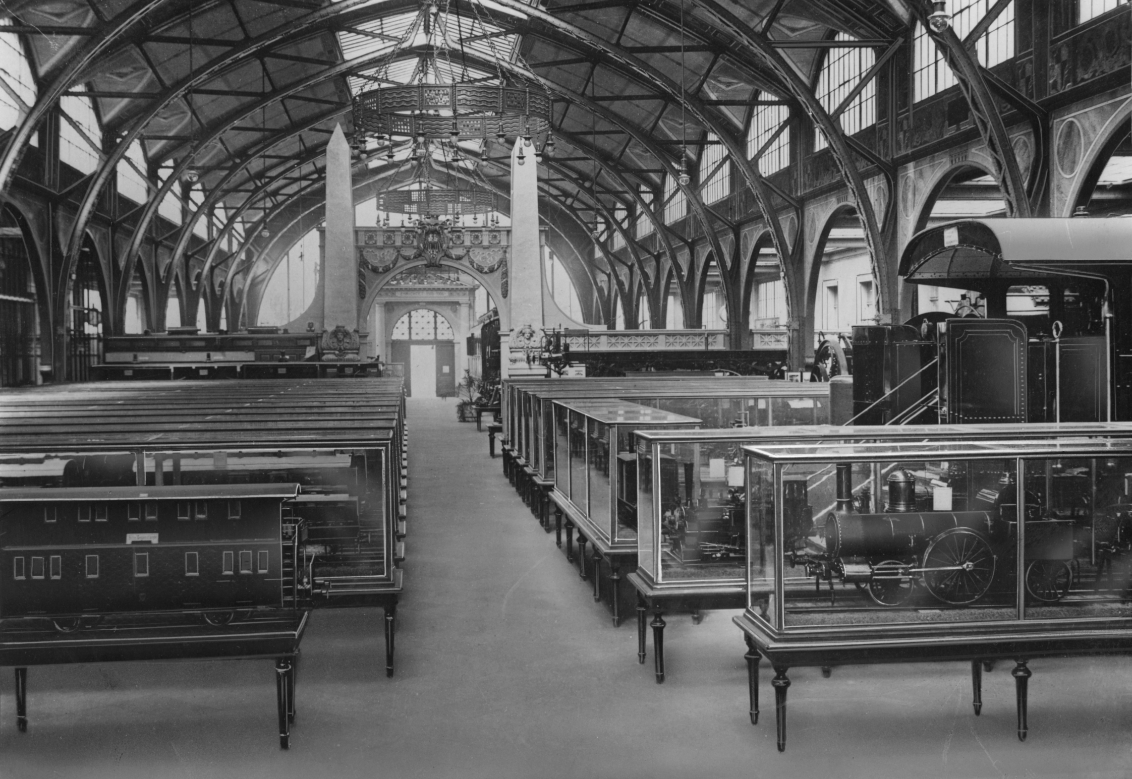 Black-and-white photo: The exhibition in the industrial hall of the former Hamburg train station. Beneath the elaborate steel-and-glass roof structure, the space is filled with display cases containing model trains.