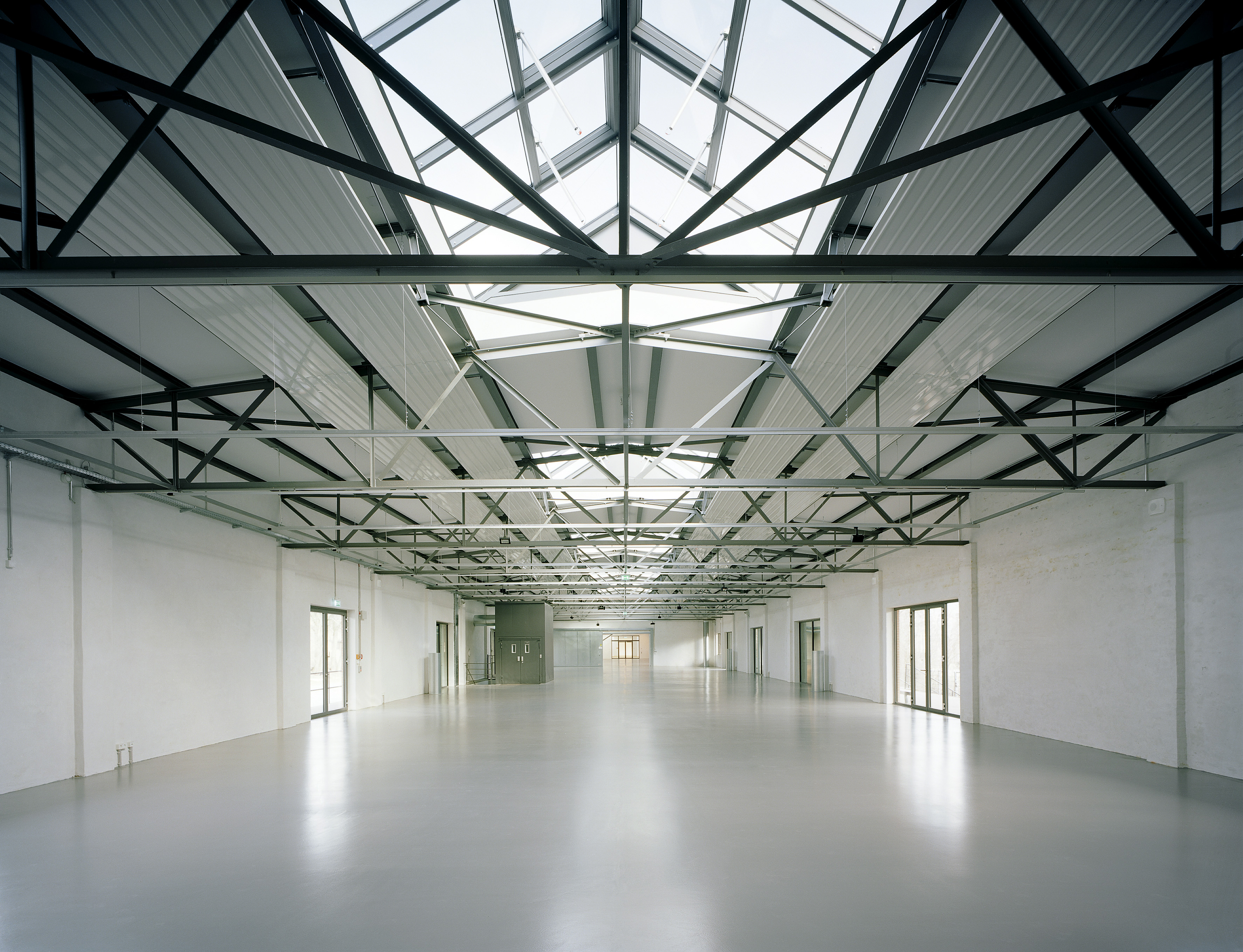 A view inside a warehouse that has obviously been recently restored: The floors and walls gleam white, and the steel ceiling structure offers a view of glass dormers.